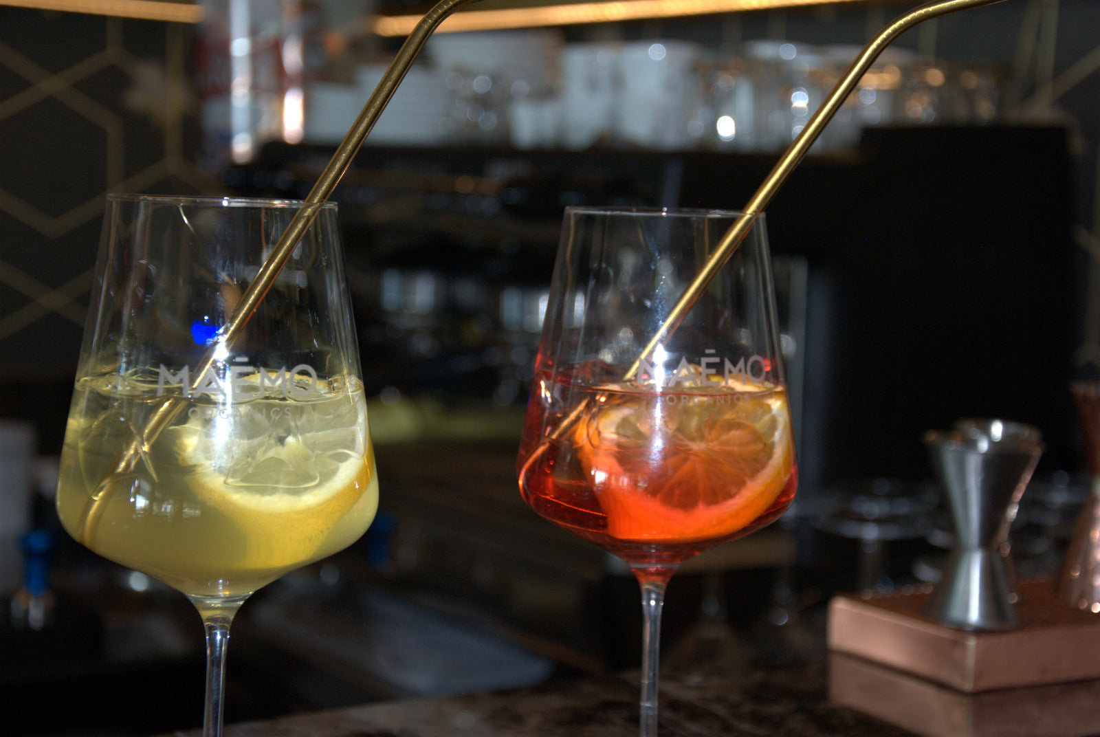 Maemo Bitter und Maemo Limoncello serviert mit Zitronen- und Orangenscheiben sowie goldenen Trinkhalmen an einer stilvollen Bar